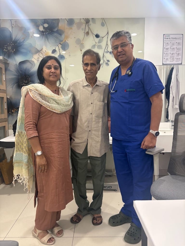 Cardiac patient and family member standing proudly with Dr. Manish Aggarwal in surgical scrubs at Yashoda Medicity